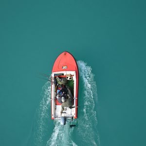 Top view of a red motorboat with fishermen navigating open turquoise waters.